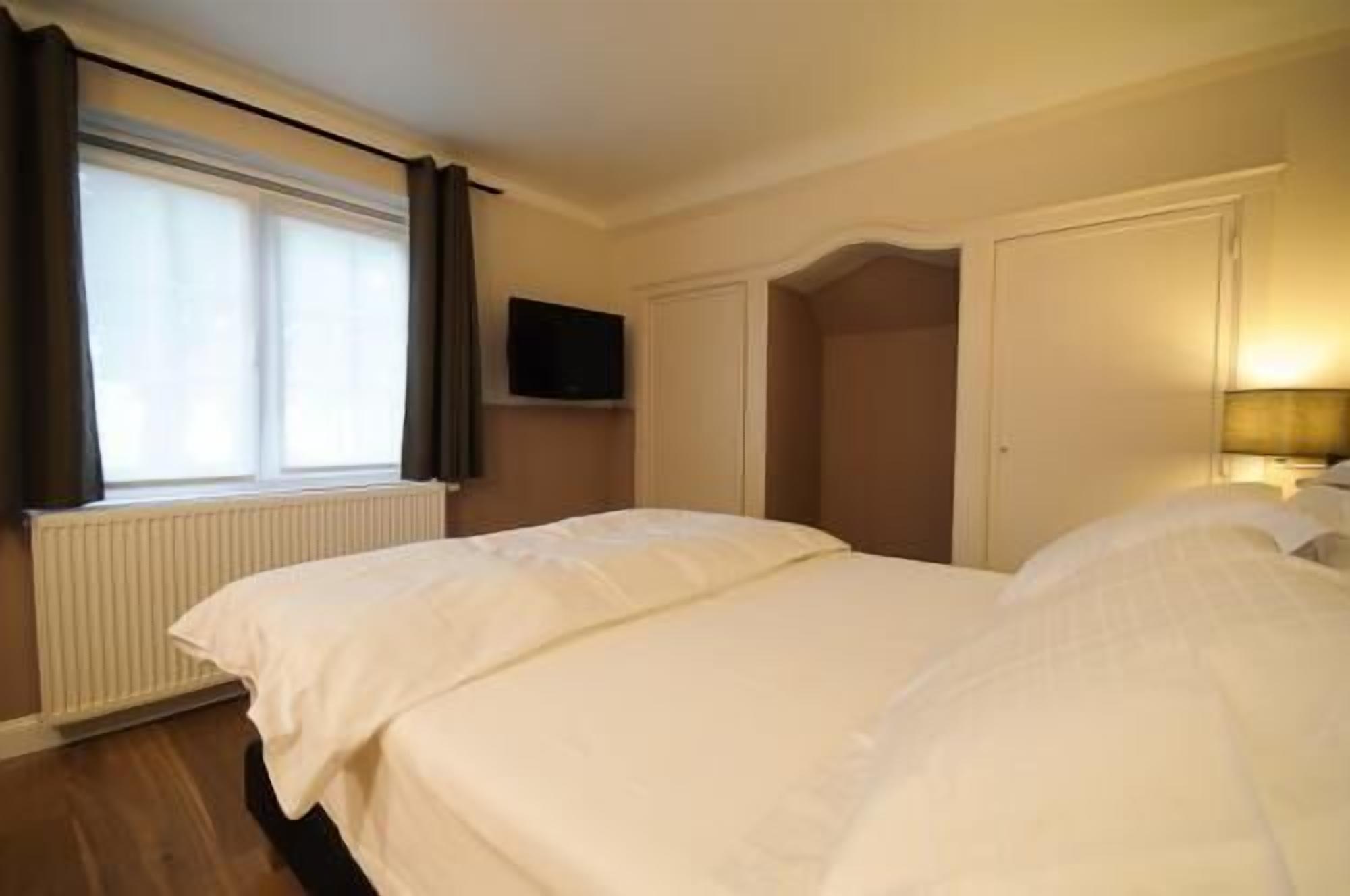 A hotel room with two beds, a television on the wall, and a window with curtains.