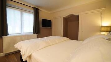 A hotel room with two beds, a television on the wall, and a window with curtains.