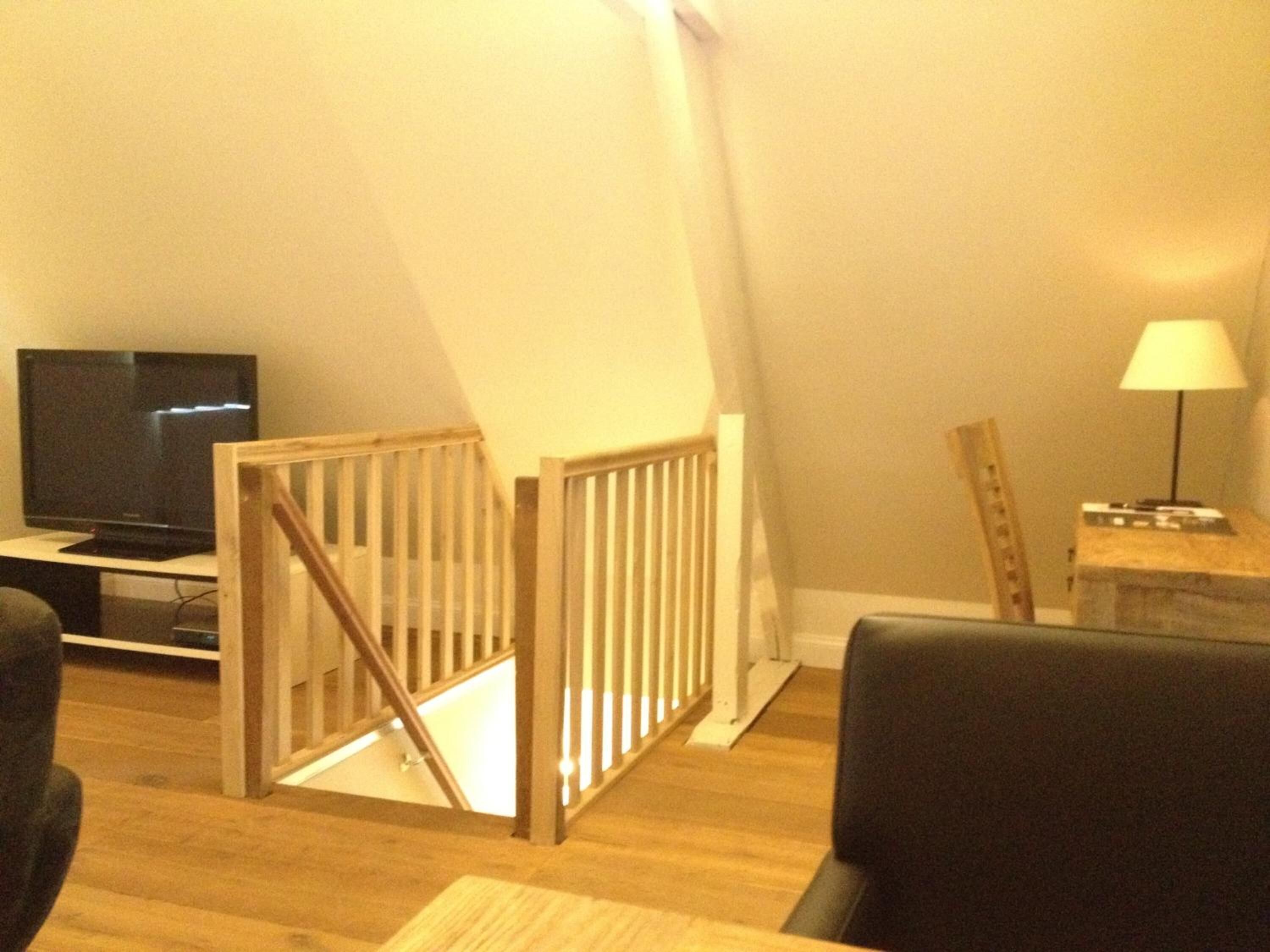 A living room with a TV, a wooden staircase, a lamp, and a chair.