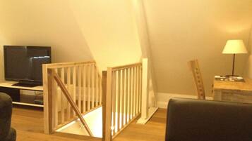 A living room with a TV, a wooden staircase, a lamp, and a chair.