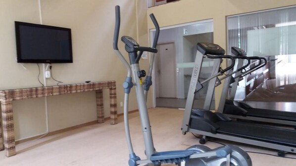Uma sala de ginástica doméstica com equipamentos de exercício, uma televisão e um banco.
