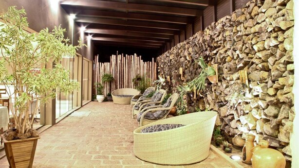 A covered outdoor seating area with wicker chairs and a woven bench, surrounded by potted plants and a stone wall. - Hotel Nascentes da Serra (Poços de Caldas)