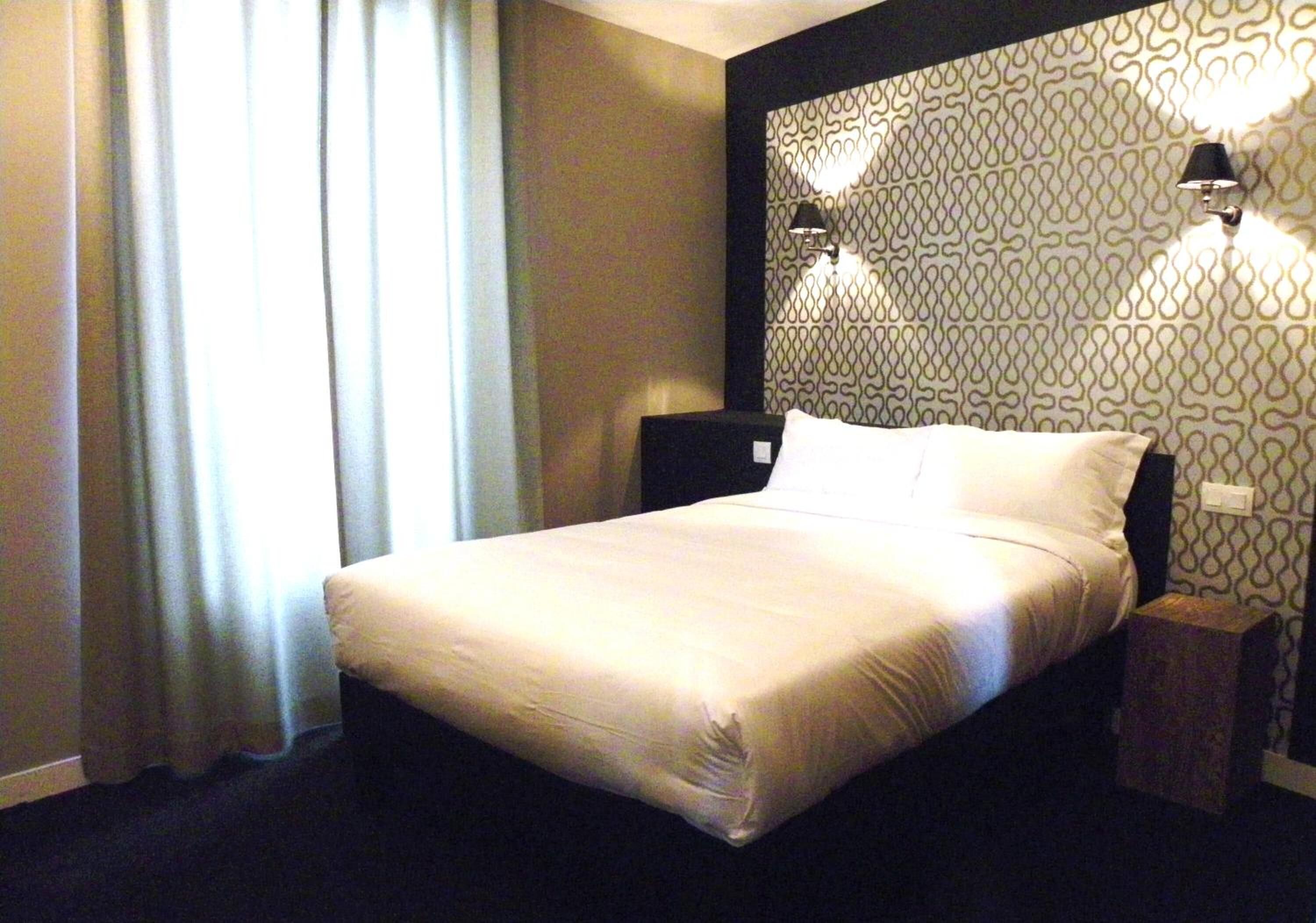 Quarto de hotel com uma cama bem arrumada, parede estampada e duas luminárias de parede.