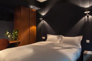 A modern bedroom with a bed, wooden paneling, a wall-mounted lamp, and a small table with flowers. - Hotel Les Terres Blanches (Chatou)