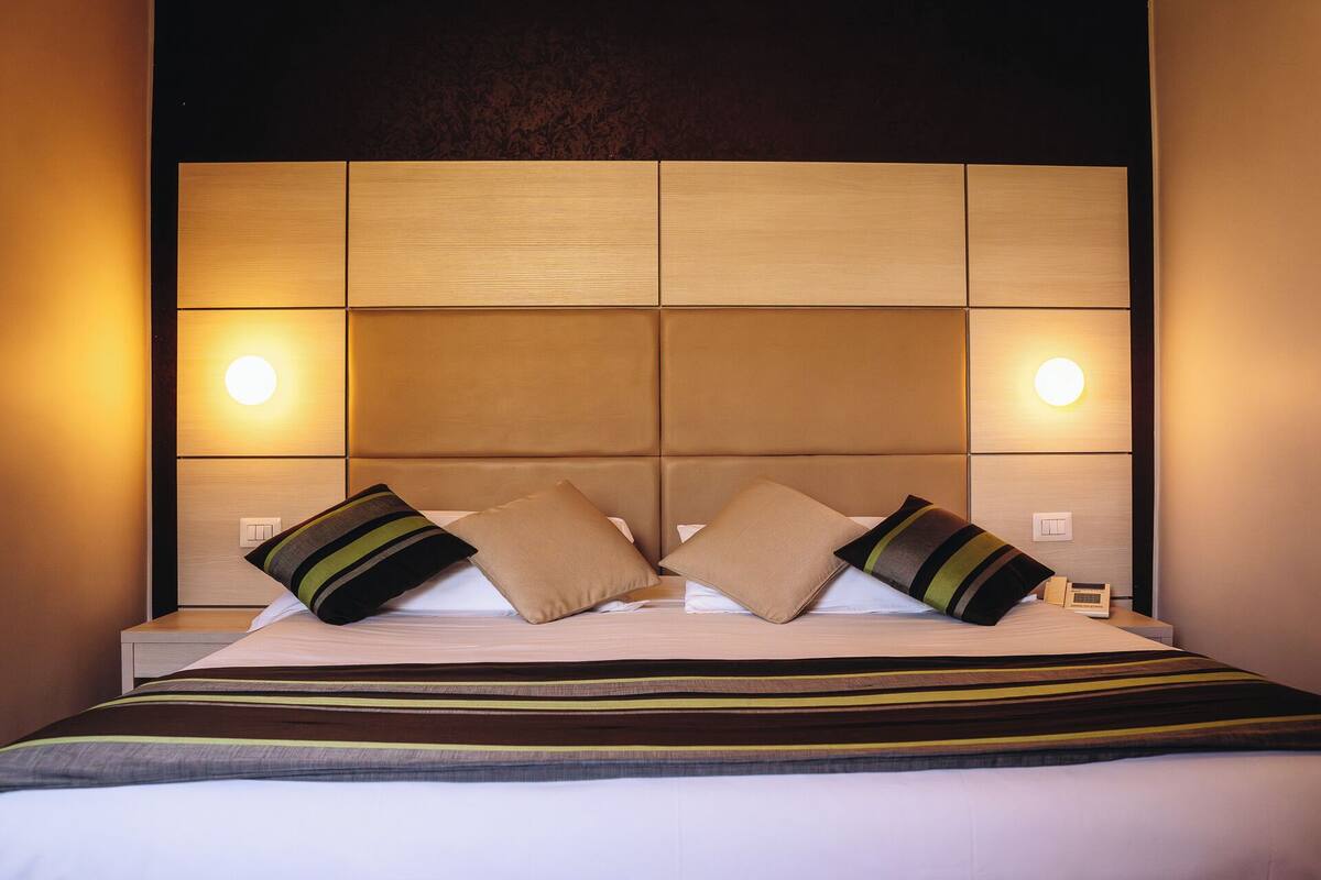 Een hotelkamer met een groot bed, een hoofdeinde met ingebouwde verlichting en twee bedlampen.