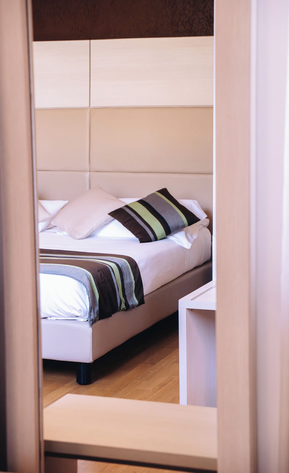 Een net opgemaakt bed met gestreepte lakens en een kussen, een nachtkastje en een houten vloer.