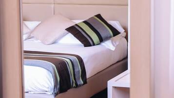 Een net opgemaakt bed met gestreepte lakens en een kussen, een nachtkastje en een houten vloer.