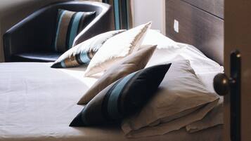 Una cama con una colcha blanca y varias almohadas, un armario de madera y una ventana con vistas a edificios.