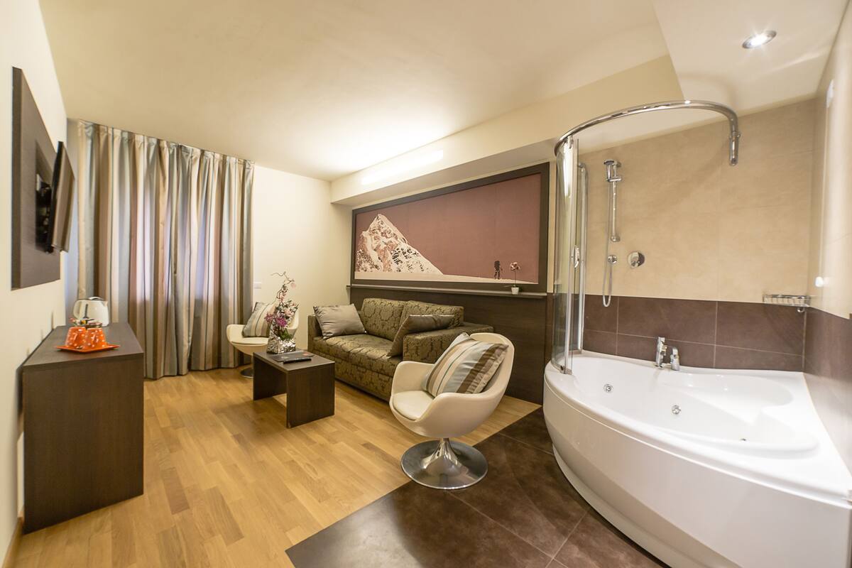 Een moderne badkamer met een groot bad, een douche en een zithoek met een bank en fauteuil.