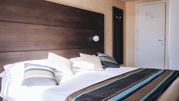 Una habitación de hotel con cabecera de madera, cama con ropa de cama a rayas, una puerta blanca y un interruptor de luz en la pared.