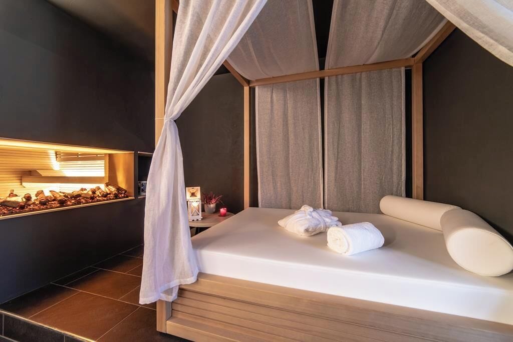 A modern hotel room with a bed, a nightstand, and a wall-mounted light.