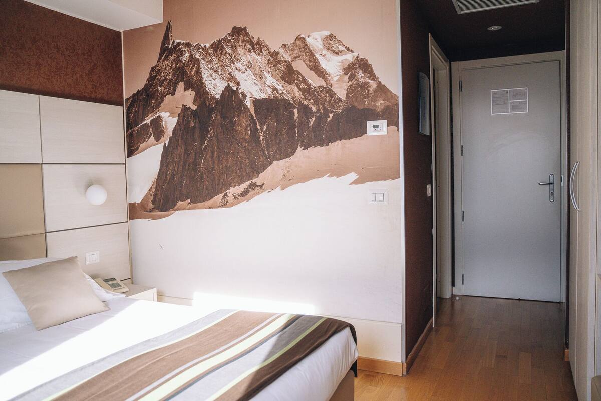 Een slaapkamer met een bed, een aan de muur bevestigd telefoontoestel en een deur naar een andere kamer.
