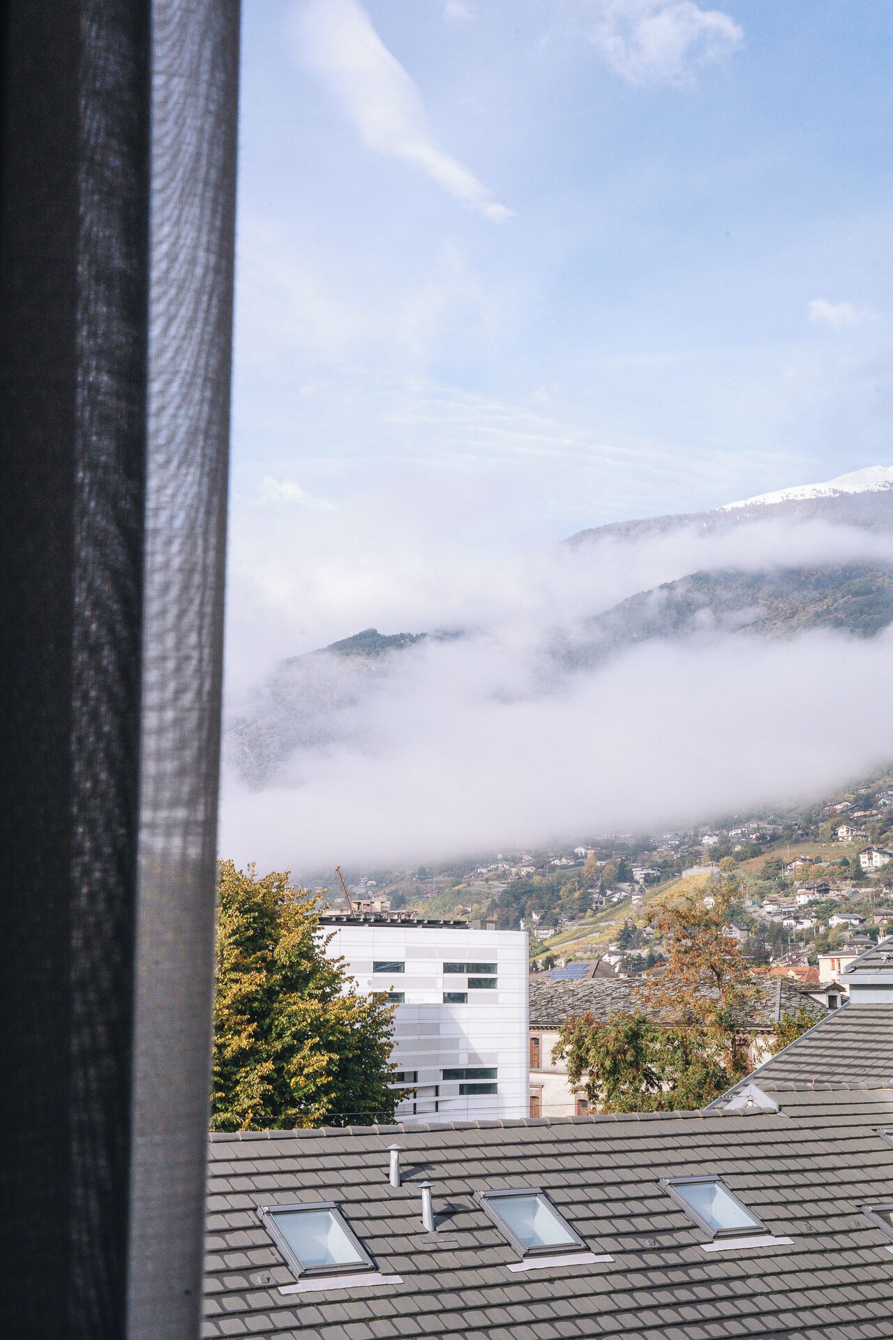 A view of a town with buildings and a mountain partially covered by clouds.