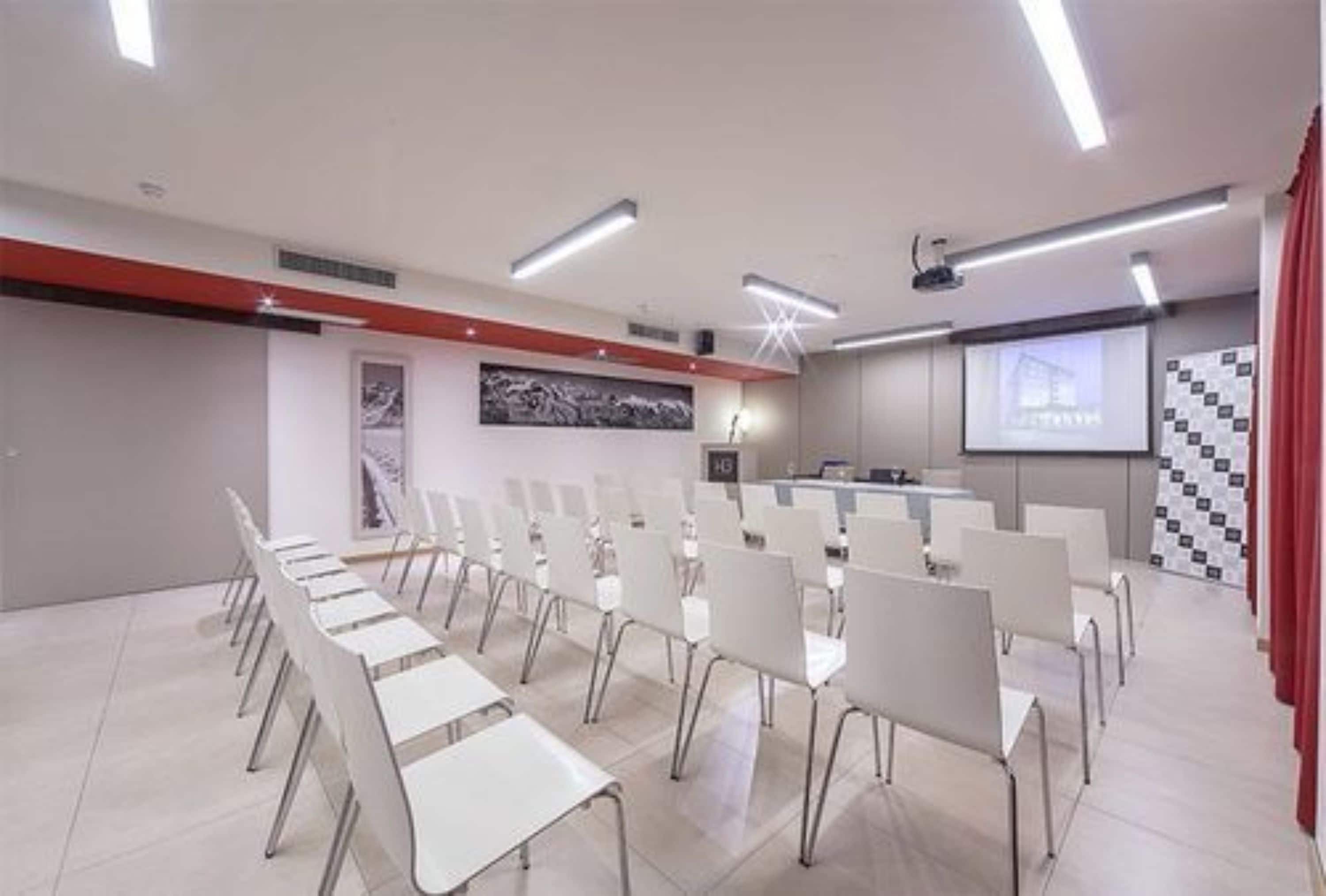 A conference room with white chairs and tables, a projector screen, and a presentation board.