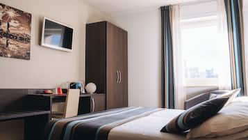 Ein Hotelzimmer mit Bett, Schreibtisch, Kleiderschrank, Fernseher und einem Fenster mit Vorhängen.