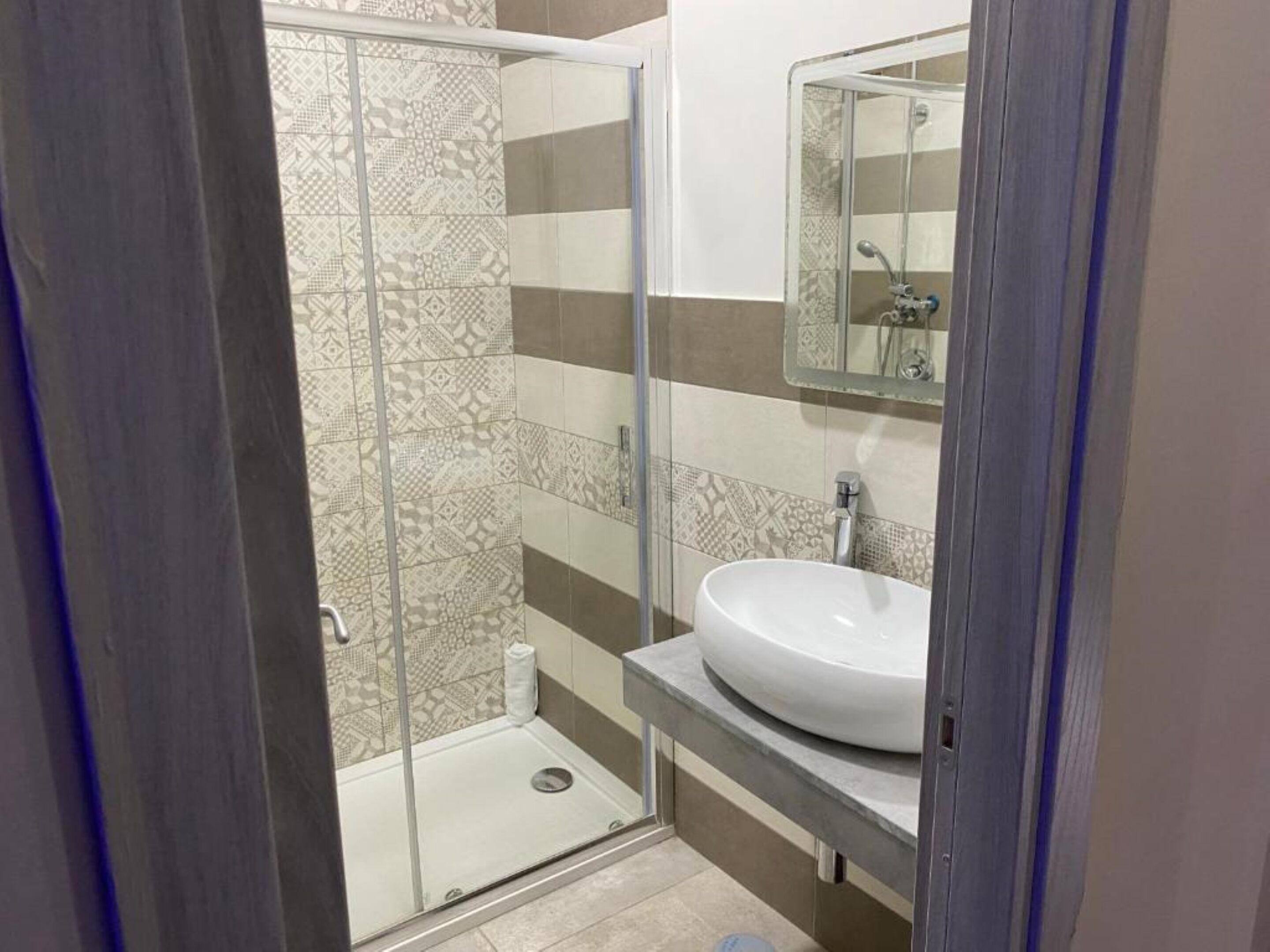 A bathroom with a glass shower enclosure, a white sink, and patterned tiles.