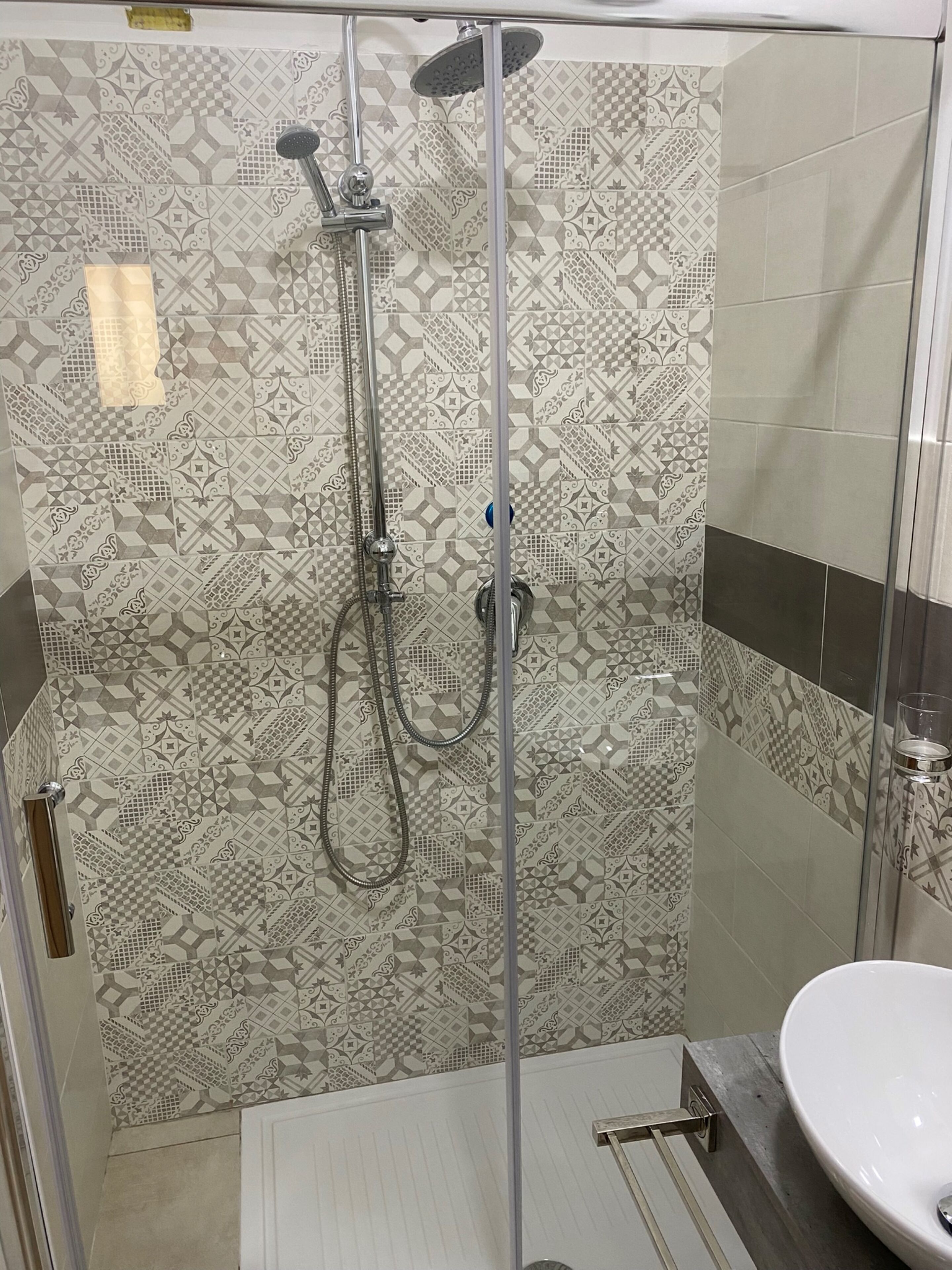 A shower with a glass door, patterned tiles, and a white sink.