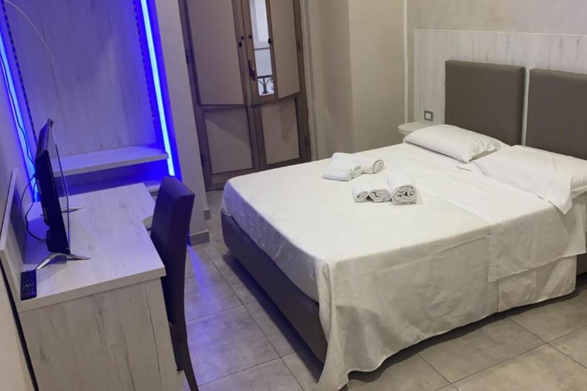 A neatly made bed with white linens and towels, a desk with a computer, and a chair.