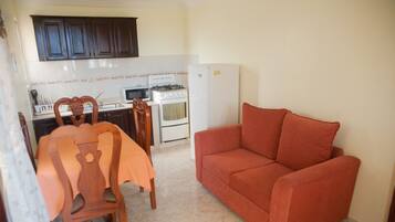 A compact kitchen with a dining table, chairs, a red sofa, and a refrigerator.