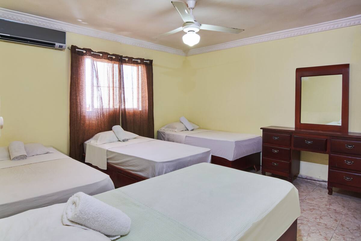 Ein Hotelzimmer mit zwei Einzelbetten, einem Holzkonsolenmöbel, einem Spiegel und einer Klimaanlage.