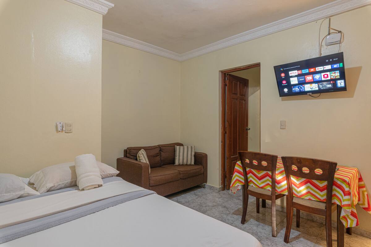 Ein Hotelzimmer mit einem Bett, einem Sofa, einem an der Wand befestigten Fernseher und einem Tisch mit Stühlen.