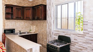 A kitchen with dark wooden cabinets, a stainless steel sink, a microwave, and a gas stove. - Tropical Island Aparthotel (Santo Domingo Este)