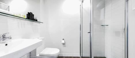 A modern bathroom with a white sink, toilet, and glass shower enclosure.
