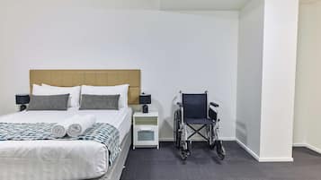 Habitación de hotel con cama, silla de ruedas, mesita de noche y lámpara.