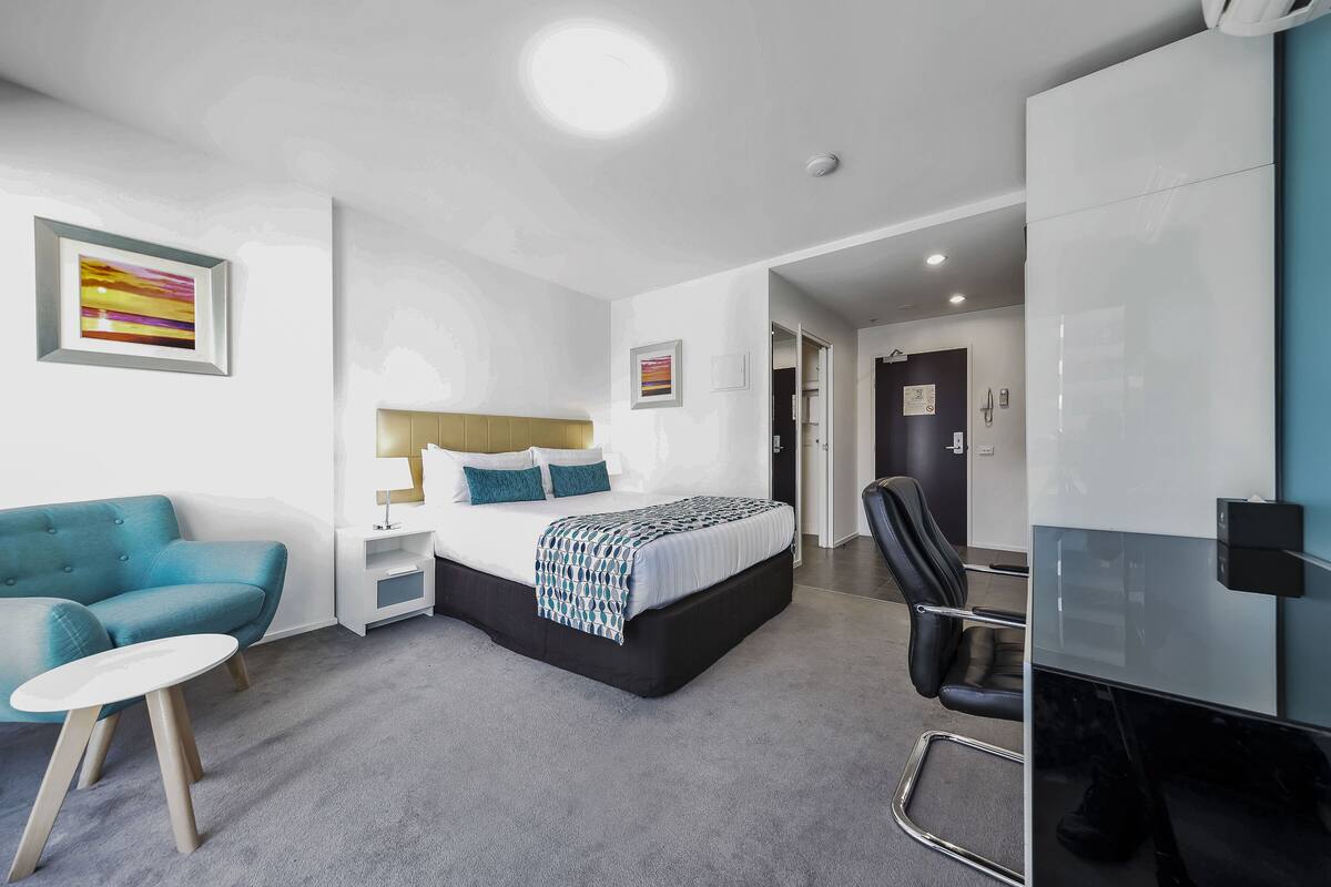 A modern hotel room with a bed, a blue sofa, a small table, and a chair.
