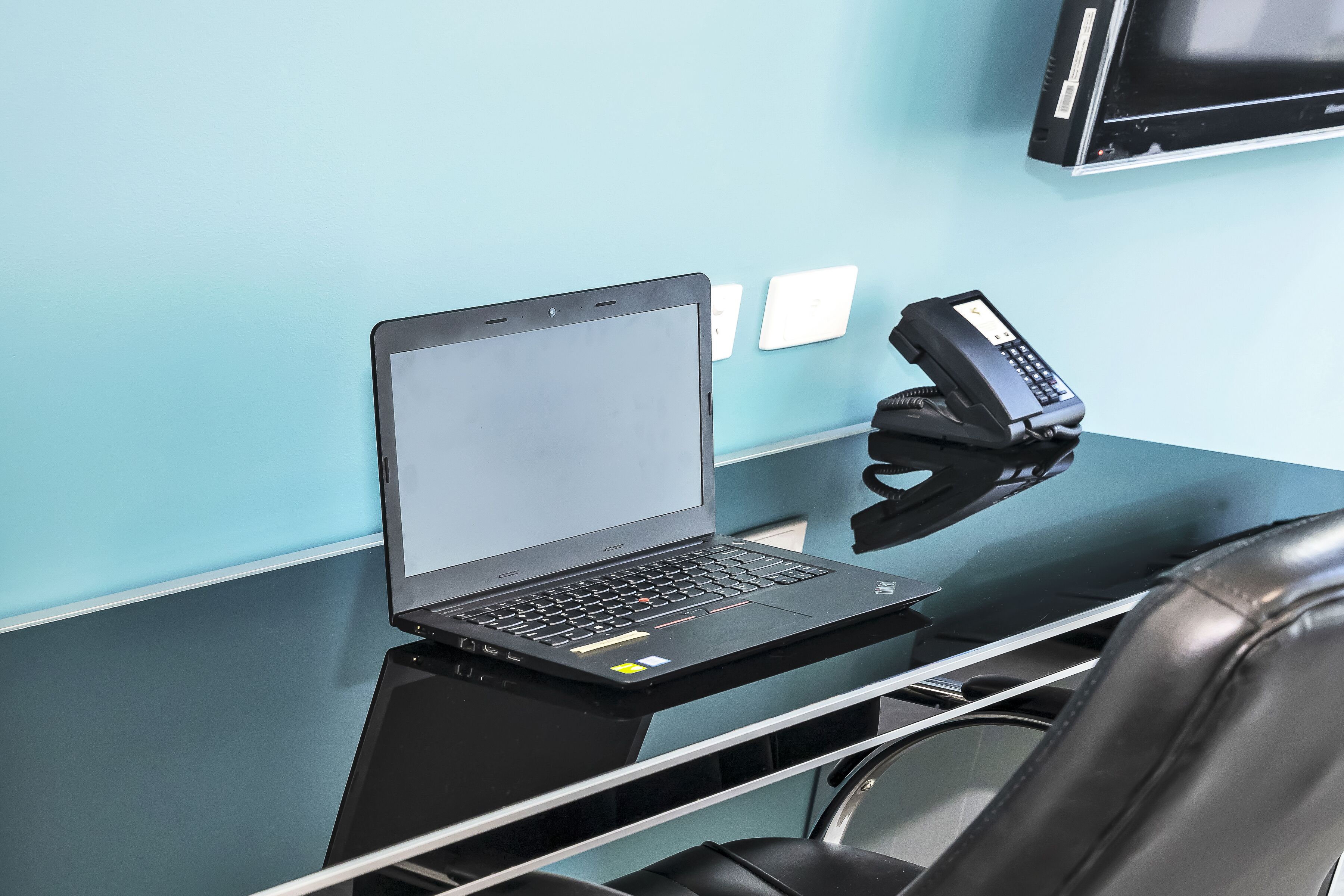 Ein Laptop auf einem schwarzen Schreibtisch mit einem Telefon und einem Stuhl.