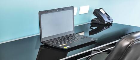 Una computadora portátil sobre un escritorio negro, con un teléfono y una silla.