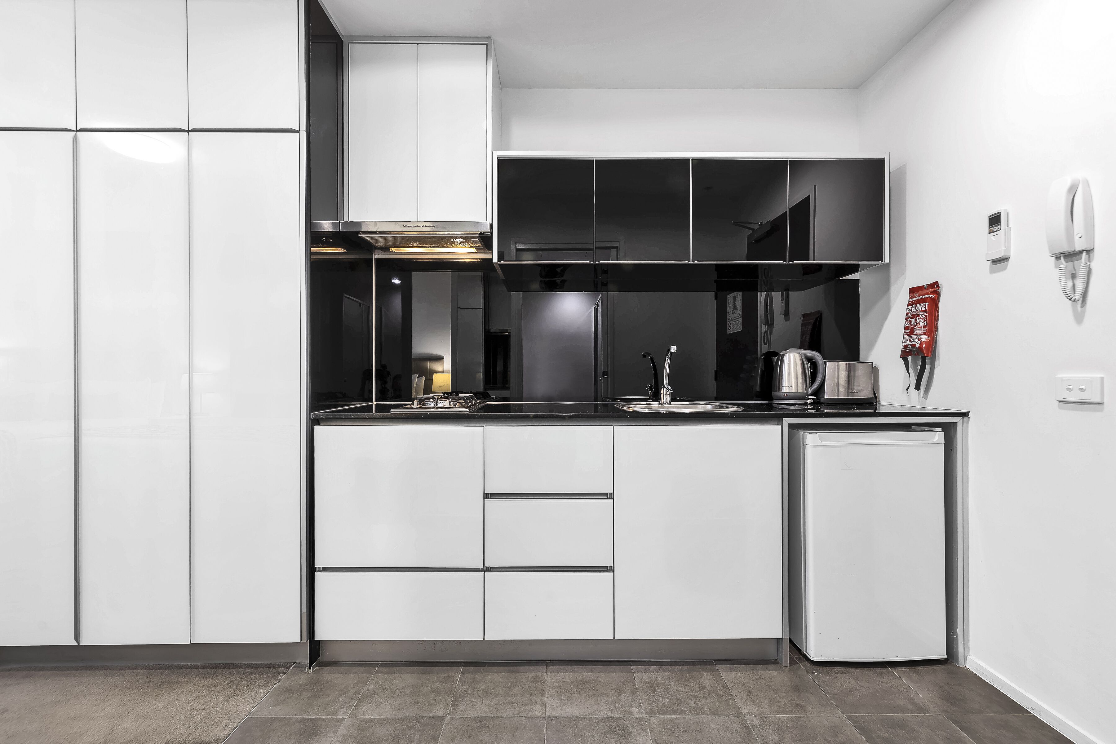 A modern kitchen with white cabinetry, a built-in stove, and a small refrigerator.