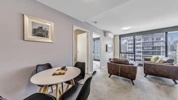 Una sala de estar moderna con comedor, ventanas amplias y vista a la ciudad, y un cuadro enmarcado en la pared.
