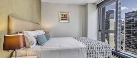Ein modernes Hotelzimmer mit großem Fenster, einem ordentlich bezogenen Bett, einem Nachttisch mit Lampe und einem gerahmten Bild an der Wand.