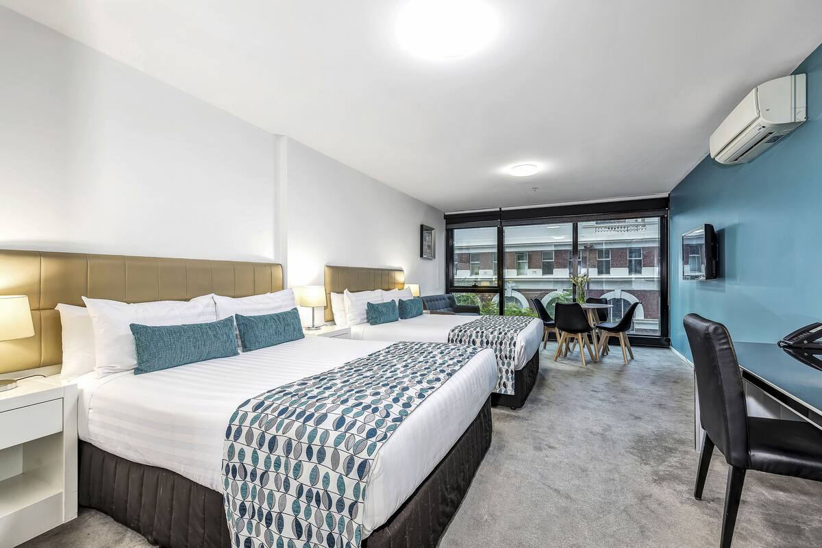 A hotel room with two beds, a desk, and a chair.