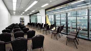 A conference room with rows of chairs, a glass wall with a city view, and a whiteboard.