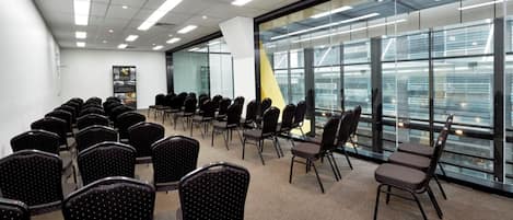 A conference room with rows of chairs, a glass wall with a city view, and a whiteboard.