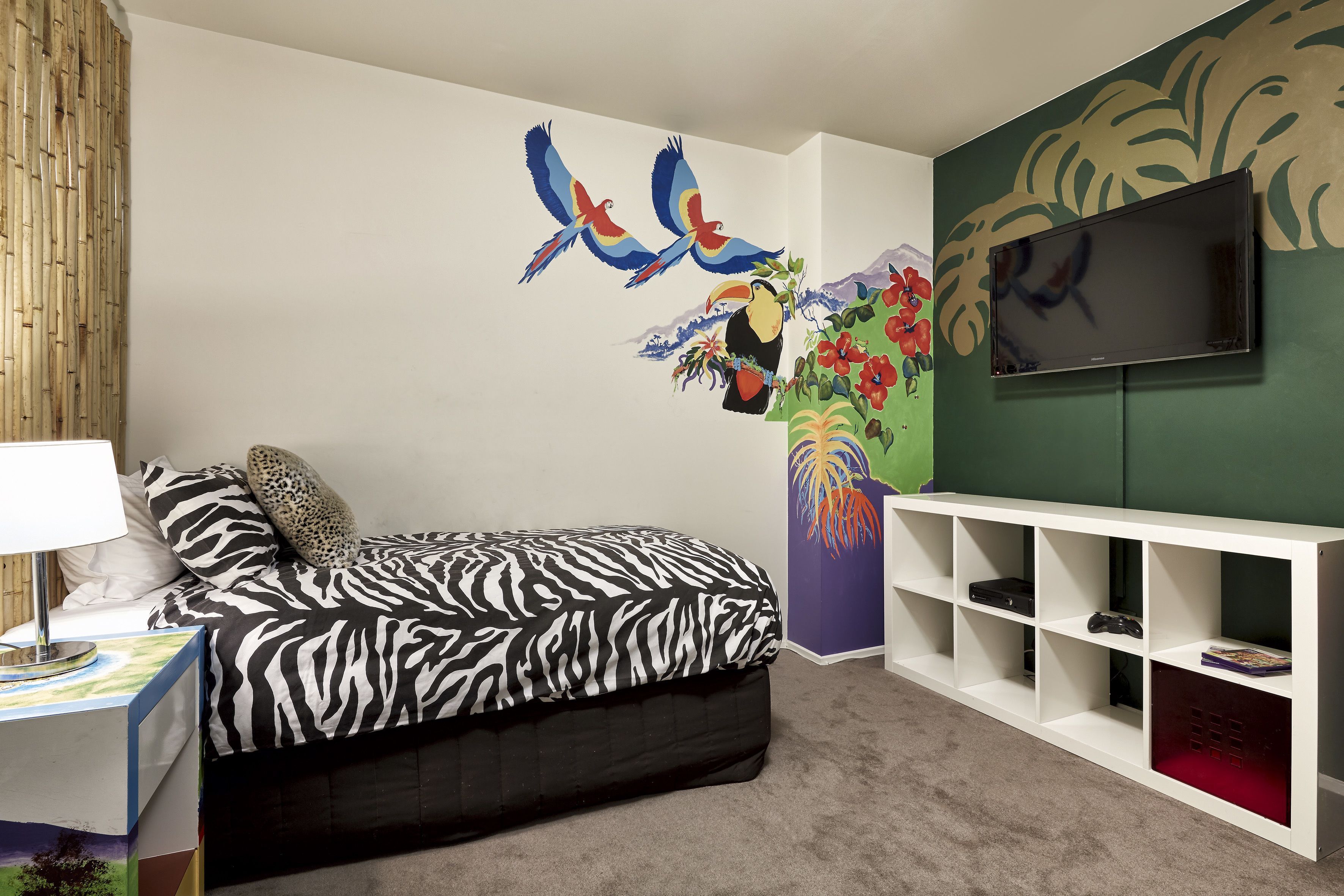 A bedroom with a zebra-patterned bed, a TV mounted on a green wall, and a white console table with shelves.