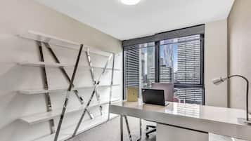 A modern office space with a desk, a laptop, and a lamp. There is a window with a view of tall buildings.
