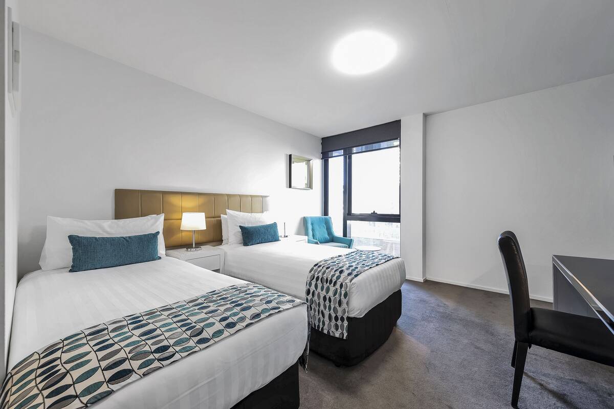 A hotel room with two beds, a desk, and a chair.