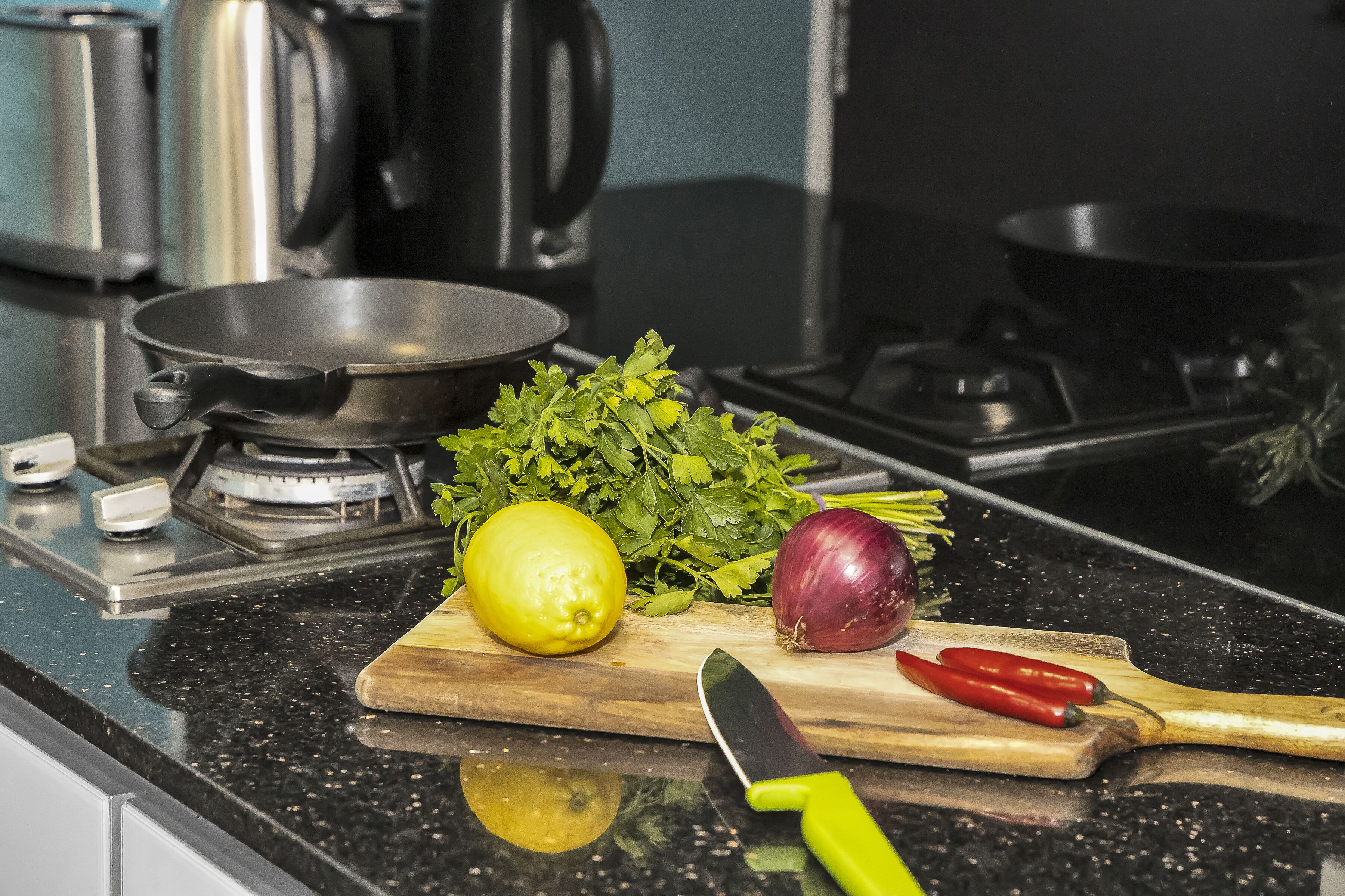 A kitchen counter with a frying pan, a lemon, a red onion, and a cutting board with a knife.