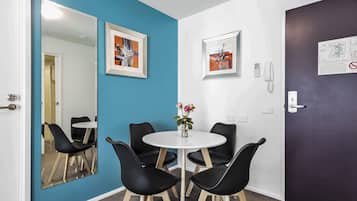 A room with a blue wall, a white door, a round table with four black chairs, and a mirror reflecting the room.