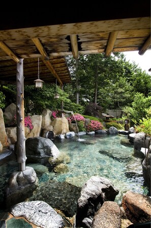 A traditional Japanese garden with a clear pond, large rocks, and pink flowers. - Yunoshimakan (Gero)