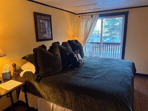 A bedroom with a large bed, a bedside table with a lamp, a framed picture on the wall, and a view of a balcony. - The Crofting Bed and Breakfast (Cloudcroft)