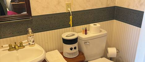 A bathroom with a sink, toilet, and a small table with a heater. There are towels on the floor and a mirror above the sink.