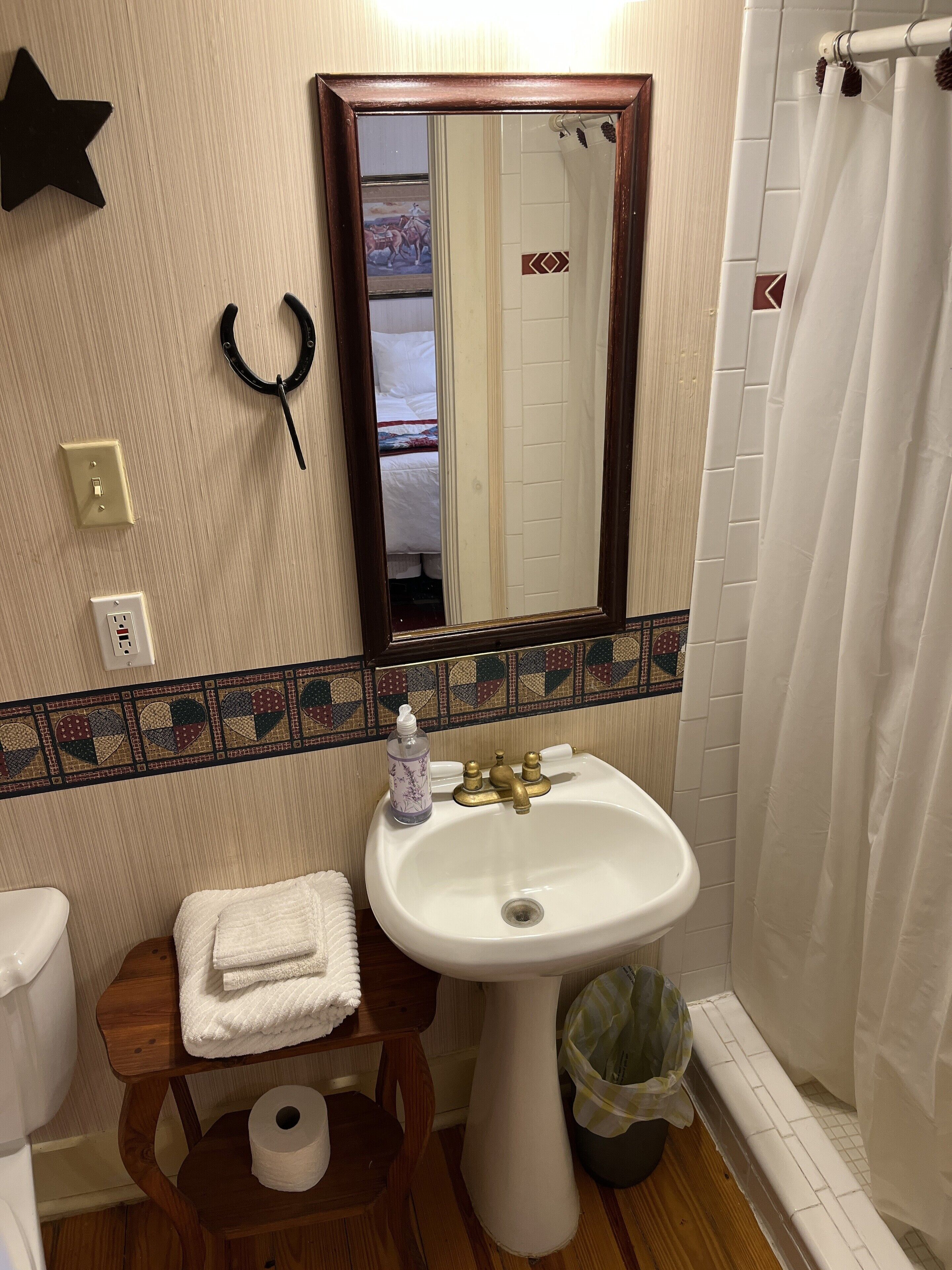 A bathroom with a white sink, a mirror, a towel rack, a star decoration, a black hair tie, a patterned tile border, and a shower curtain.