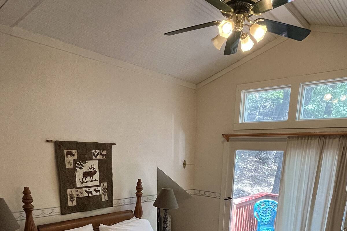 A bedroom with a bed, a ceiling fan, a window, and a view of a balcony.