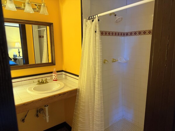 A bathroom with a sink, mirror, and shower.