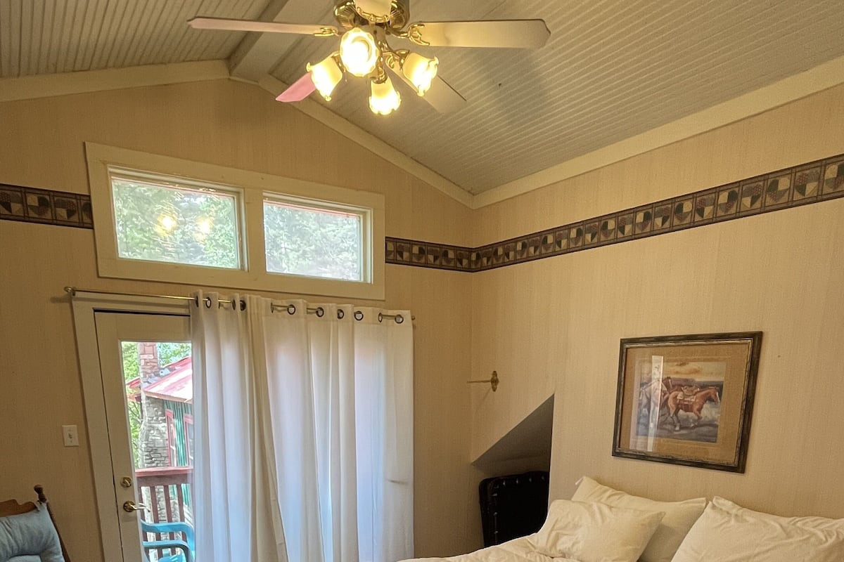 A bedroom with a bed, a chair, a ceiling fan, a window, and a door.