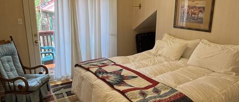 A bedroom with a bed, a chair, a ceiling fan, a window, and a door.